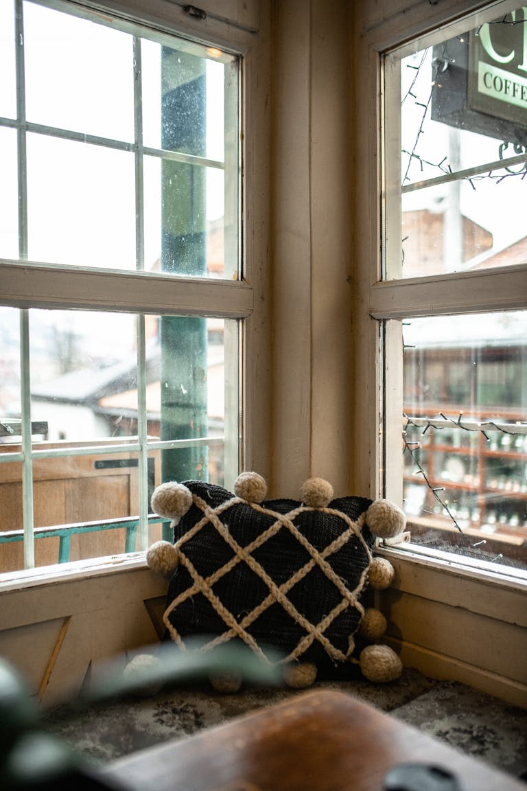 A cozy cafe corner with a geometric pillow by the window, inviting relaxation.