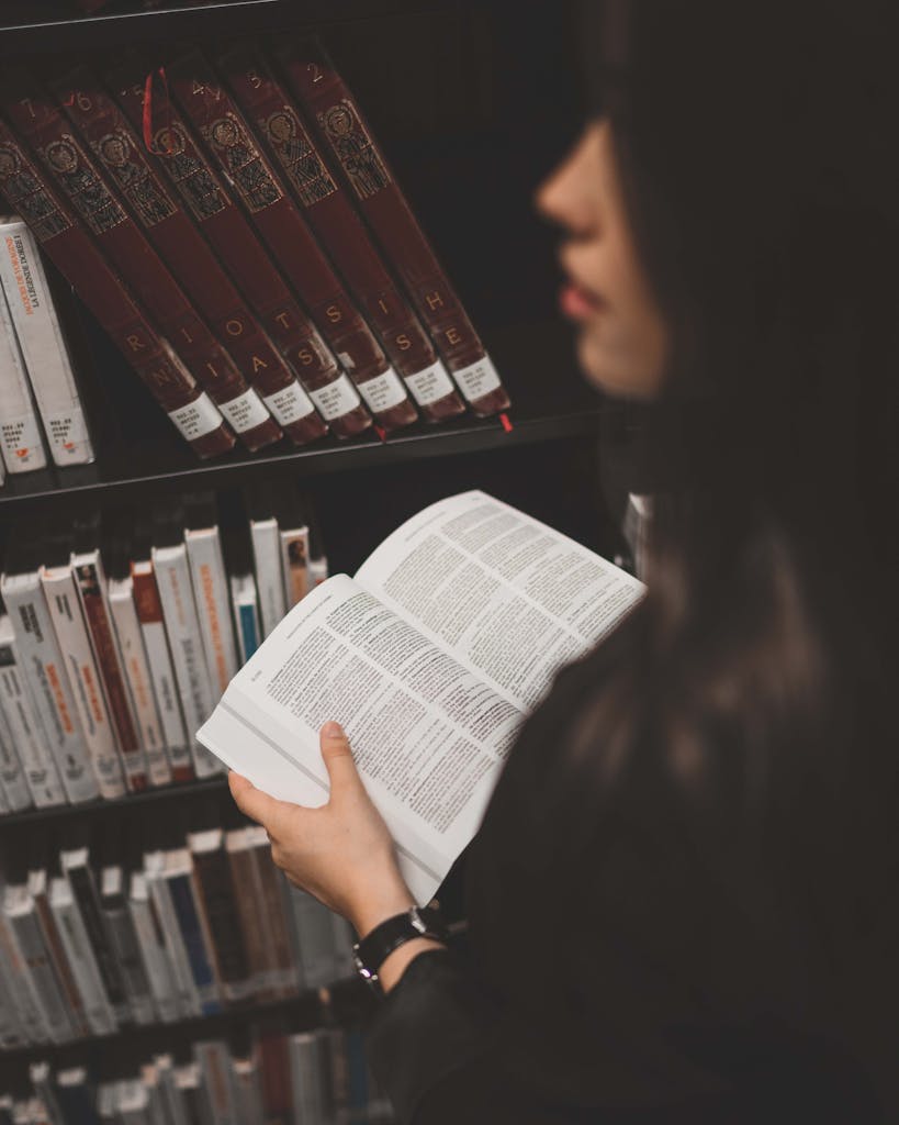 Focused woman reads a book in a cozy library, surrounded by bookshelves.