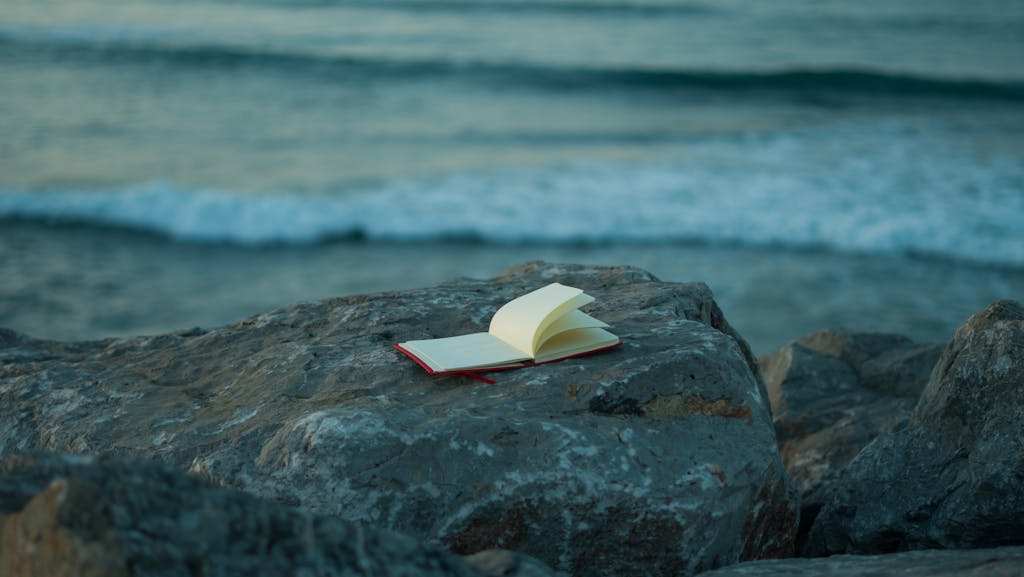Open forgiveness journal on a rocky coastline overlooking the ocean waves at dusk. A peaceful scene for reflection.