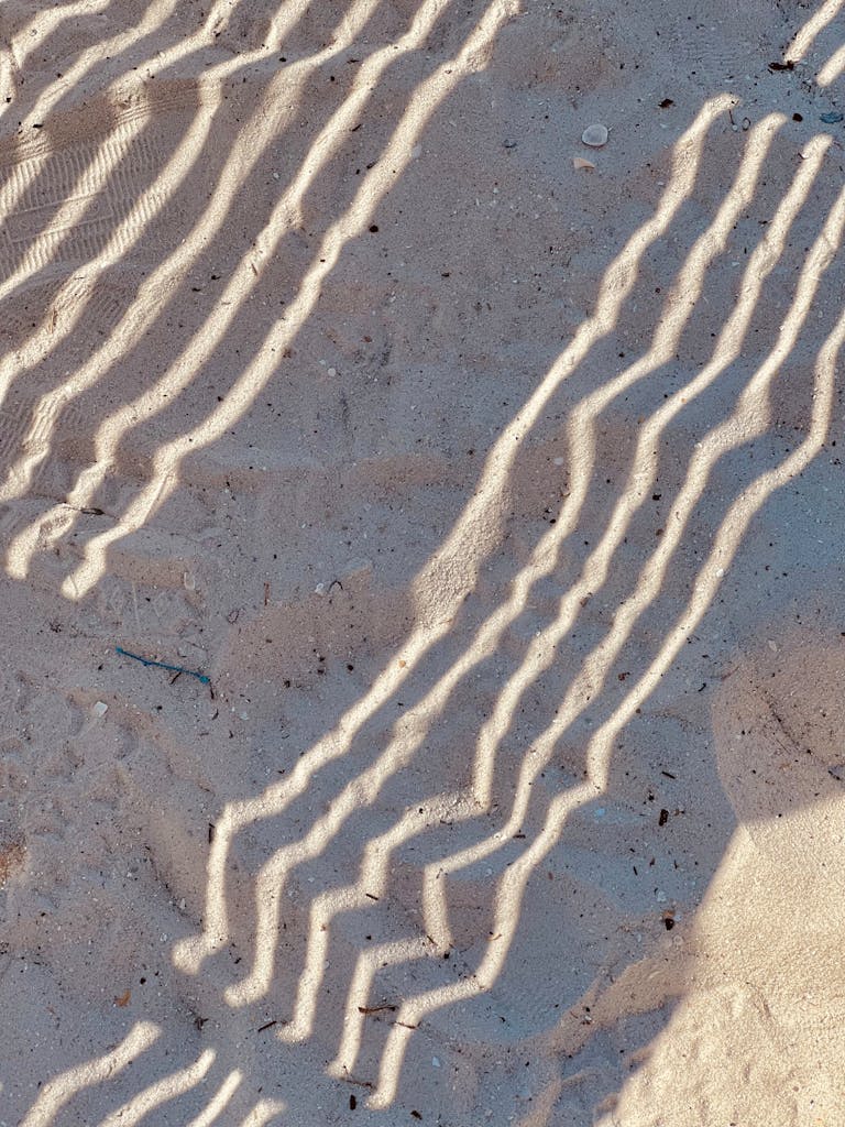 Wavy shadows create unique patterns on a sandy seashore, offering a natural abstract design.