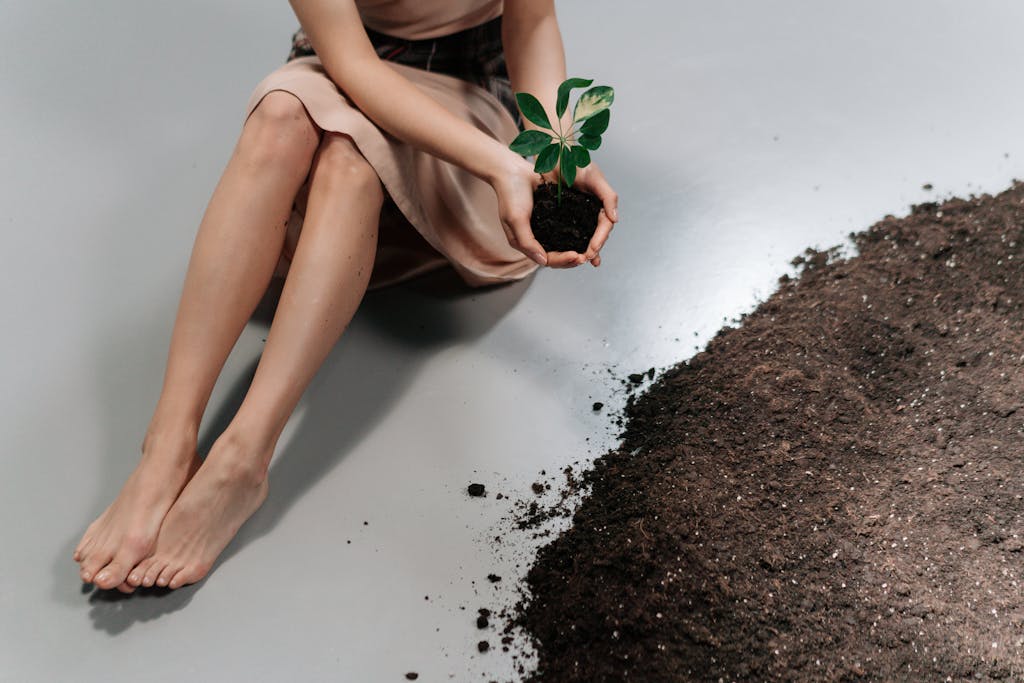 A woman sits with a seedling in her hands, symbolizing growth and environmental care.