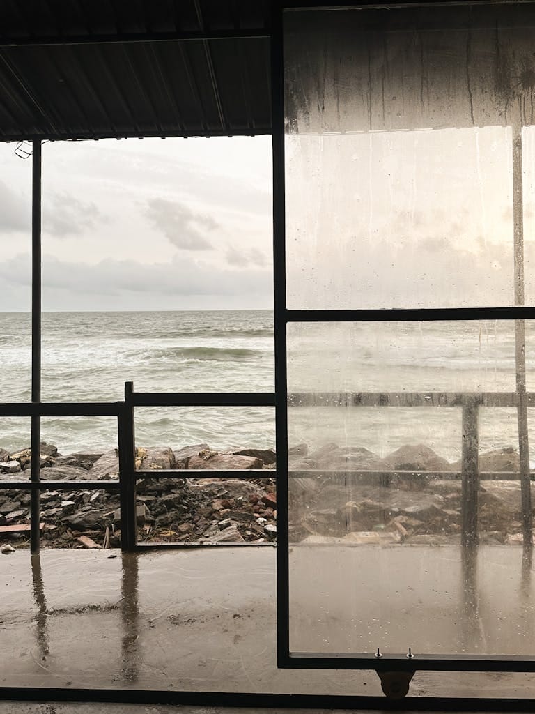 An image of a rainy day view of the ocean through a transparent, wet window by a rustic outdoor structure, meant to symbolize the rainy days in our minds.