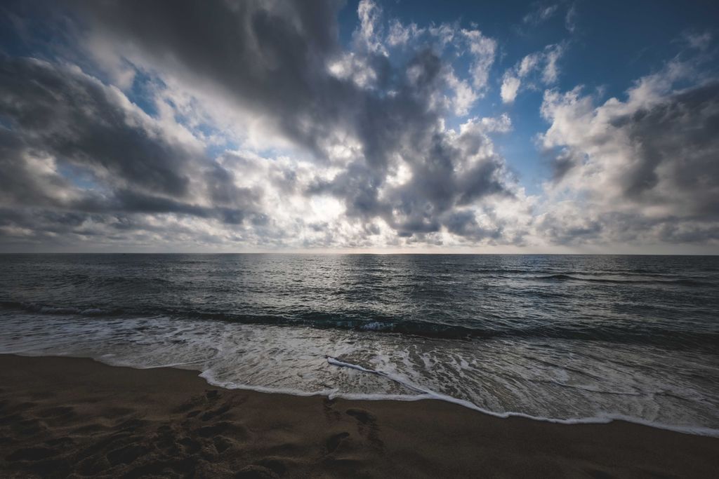 Breathtaking view of foamy waves of ocean on sandy beach at cloudy sunset