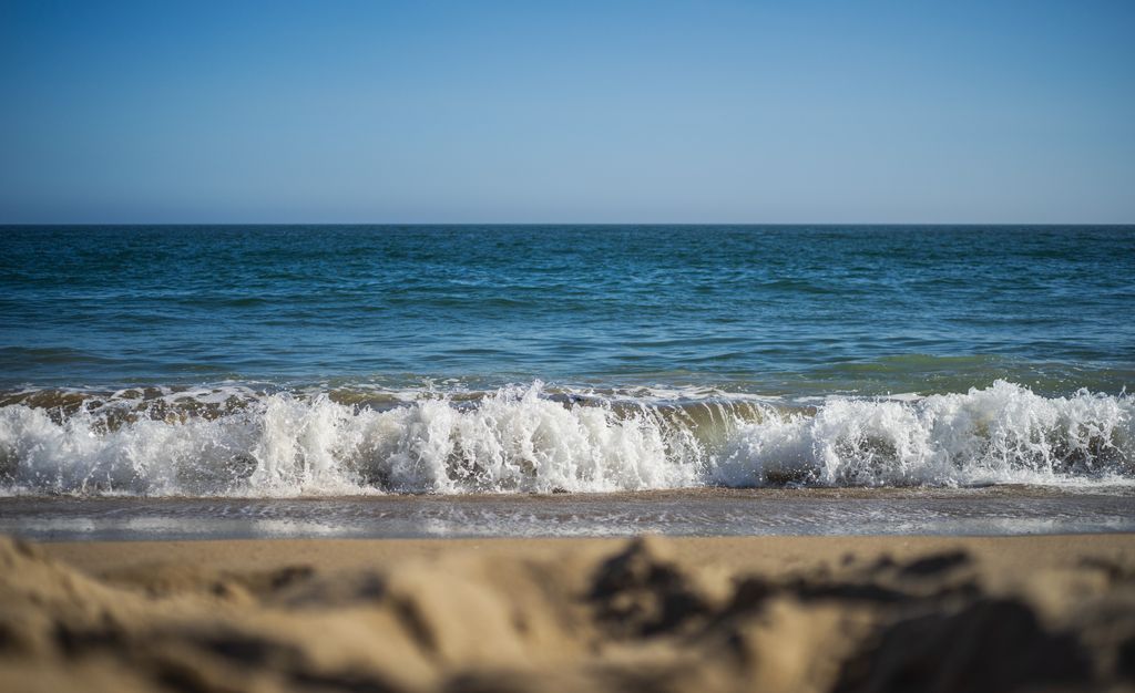 Capture of a tranquil beach scene with waves crashing on a sandy shore under a clear blue sky.