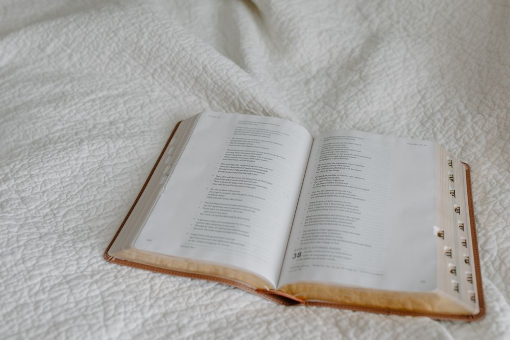 An open Bible resting on a textured white quilt, creating a serene atmosphere for someone to rest without feeling guilty.