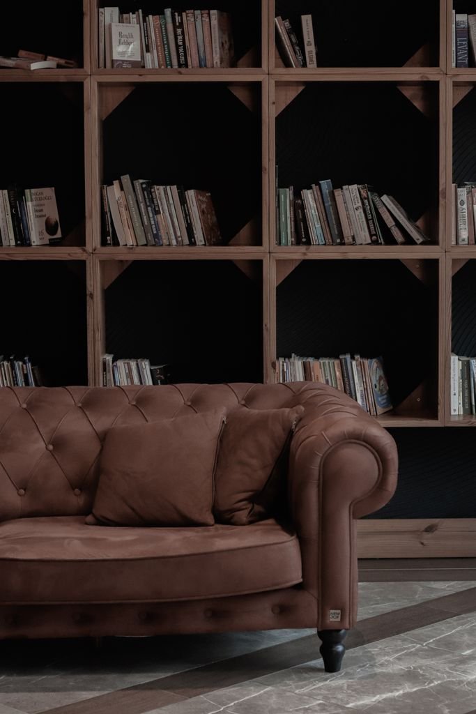 Luxurious leather sofa in a warm, elegant library setting with wooden bookshelves filled with books.