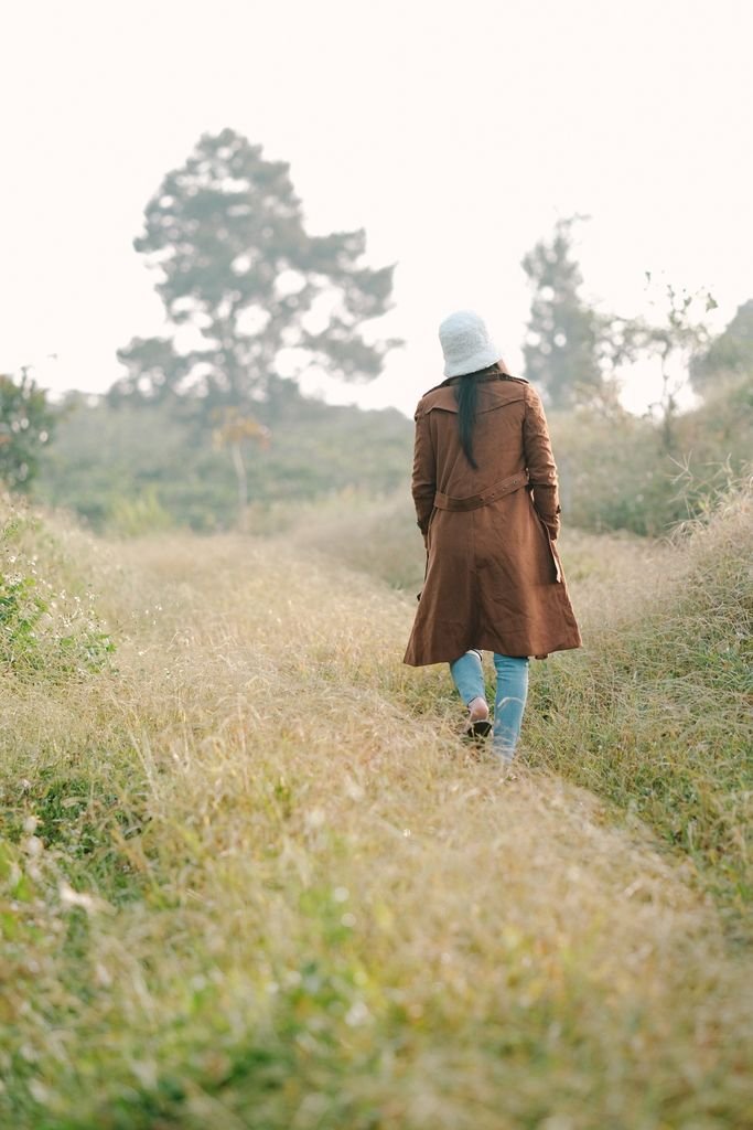 Woman in a brown coat walking through a grassy path surrounded by nature on a calm day, healed from church hurt.