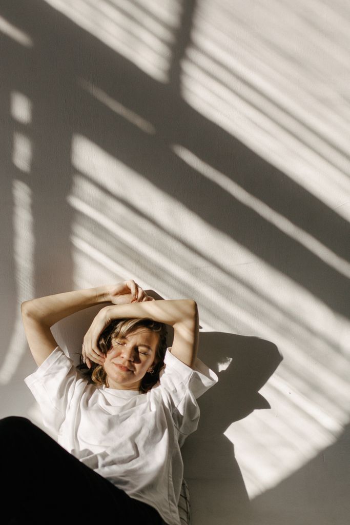 Woman lounging in sunlight, casting soft shadows in a minimalist setting.
