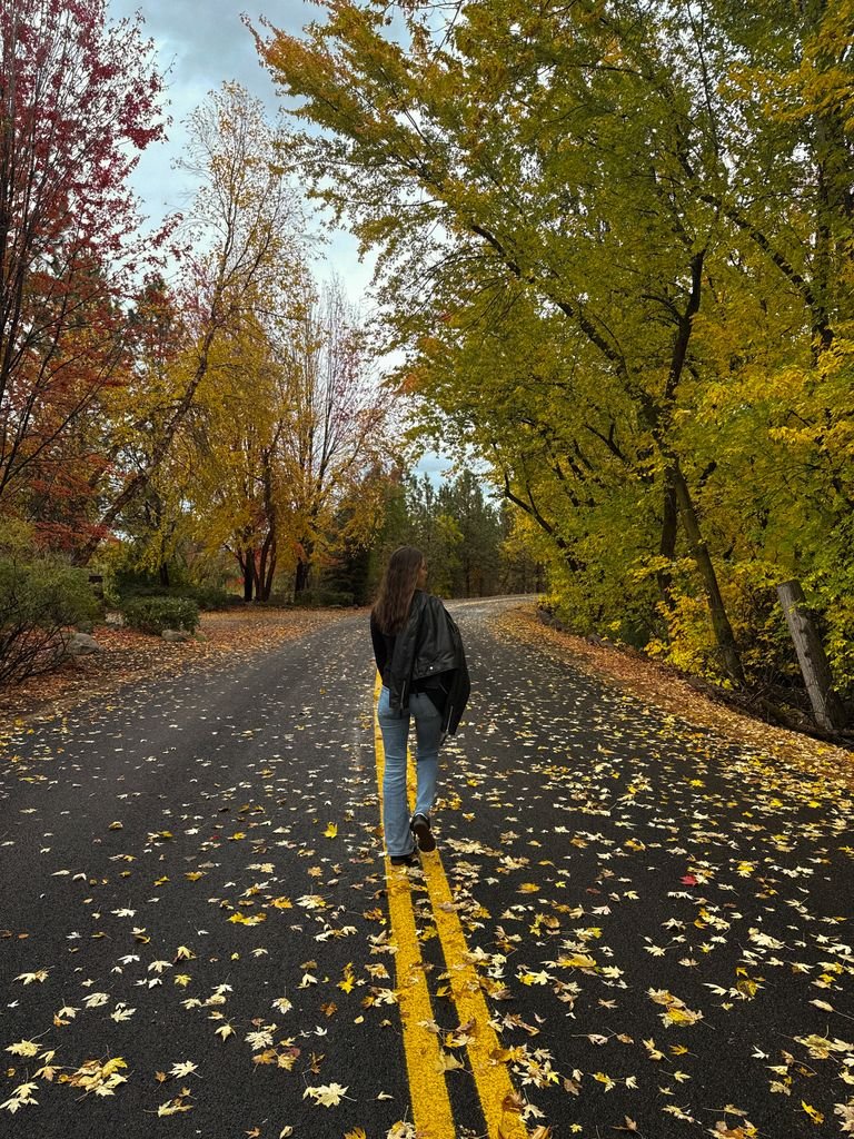 Woman walking along a scenic autumn road, surrounded by colorful fall foliage.