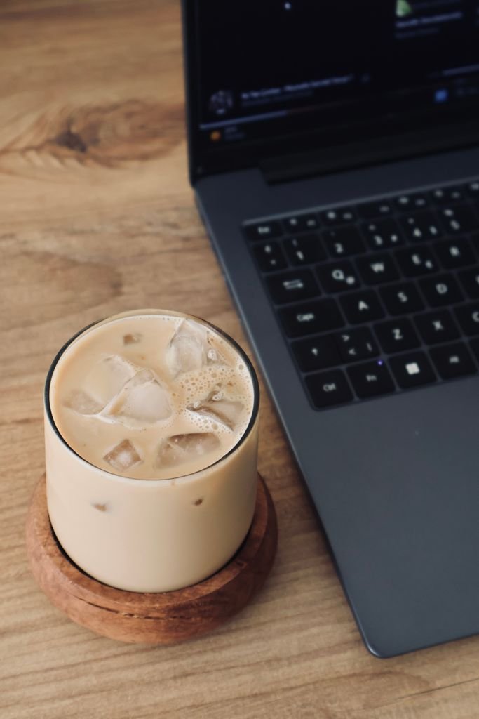 Biblical Mindset & Behavioral Coaching : Refreshing iced coffee in glass near laptop on wooden desk, cozy workspace vibe.