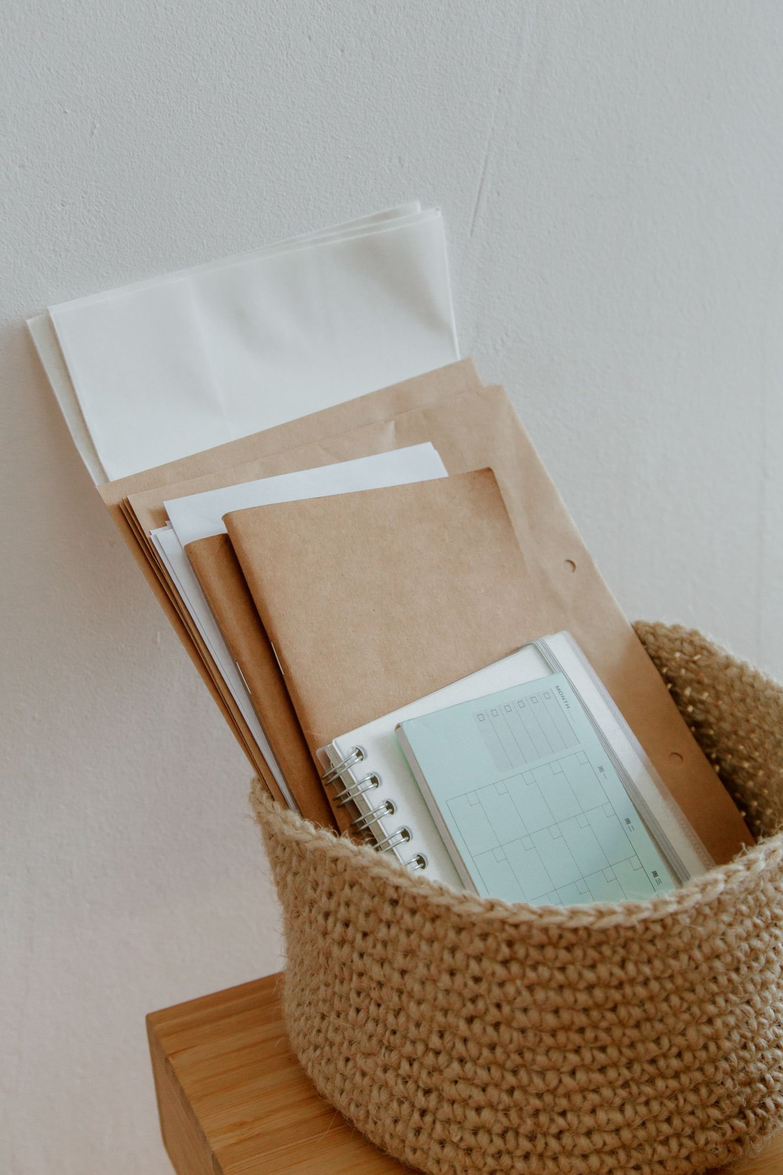Woven basket filled with notebooks, papers, and office supplies on a wooden desk.